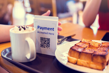 Naklejka na ściany i meble Selective focus to QR code payment tag with blur bread set meal and coffee in coffee shop or restaurant to accepted generate digital pay without money. Qr code payment concept.