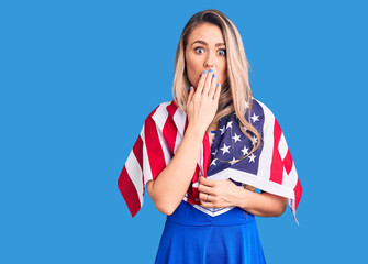 Young beautiful blonde woman wearing cheerleader uniform and united states flag covering mouth with...