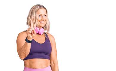 Middle age fit blonde woman wearing gym clothes and using headphones showing and pointing up with finger number one while smiling confident and happy.