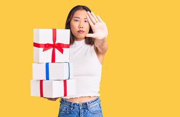 Young beautiful chinese girl holding gift with open hand doing stop sign with serious and confident expression, defense gesture