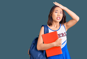 Young beautiful chinese girl wearing cheerleader uniform and student backpack holding binder...
