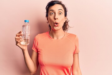 Young beautiful hispanic woman drinking bottle of water scared and amazed with open mouth for surprise, disbelief face