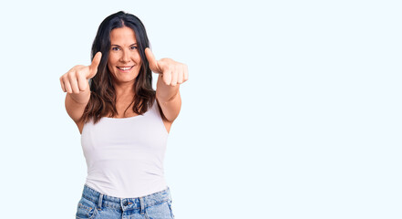 Obraz na płótnie Canvas Young beautiful brunette woman wearing casual sleeveless t-shirt approving doing positive gesture with hand, thumbs up smiling and happy for success. winner gesture.