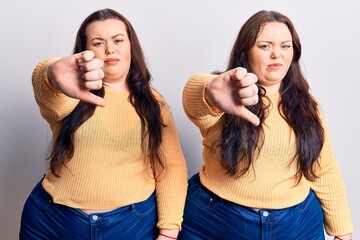 Young plus size twins wearing casual clothes looking unhappy and angry showing rejection and negative with thumbs down gesture. bad expression.