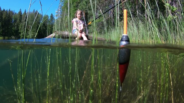 Little girl fishing on a green forest lake's coast with underwater view of fishing float and weed on a bottom