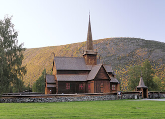 Fototapeta na wymiar Beautiful Wooden Stave Church Of Lom Surrounded By Mountains And Trees At Jotunheimen National Park On A Sunny Summer Day With A Clear Blue Sky