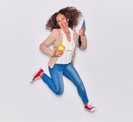 Young beautiful hispanic businesswoman wearing elegant clothes celebrating with open mouth. Jumping excited holding cup of coffee and clipboard over isolated white background
