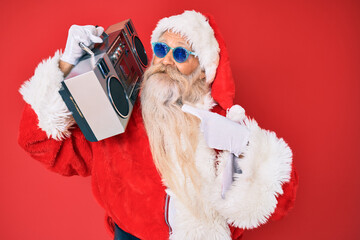 Old senior man wearing santa claus costume and boombox smiling happy pointing with hand and finger