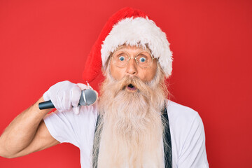 Fototapeta na wymiar Old senior man with grey hair and long beard wearing santa claus costume singing with microphone scared and amazed with open mouth for surprise, disbelief face
