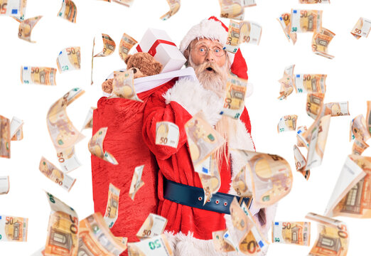 Old senior man with grey hair and long beard wearing santa claus costume holding bag with presents scared and amazed with open mouth for surprise, disbelief face