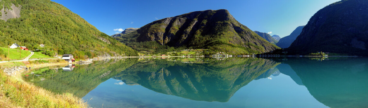 Panorama Of Mountains Reflecting In The Calm Water Of The Dalsfjord Near Skjolden On A Sunny Summer Day With A Clear Blue Sky And A Few Clouds