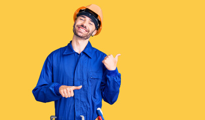 Young hispanic man wearing worker uniform pointing to the back behind with hand and thumbs up, smiling confident