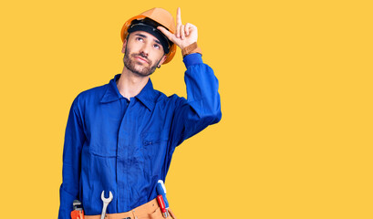 Young hispanic man wearing worker uniform making fun of people with fingers on forehead doing loser gesture mocking and insulting.