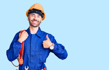 Young hispanic man wearing elecrician uniform holding cable smiling happy and positive, thumb up...