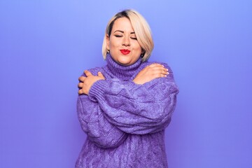 Beautiful blonde plus size woman wearing casual turtleneck sweater over purple background Hugging oneself happy and positive, smiling confident. Self love and self care