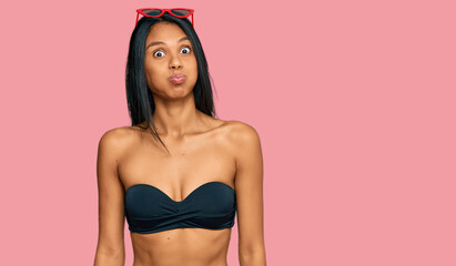 Young african american woman wearing bikini puffing cheeks with funny face. mouth inflated with air, crazy expression.