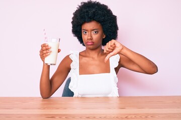 Young african american woman holding glass of milk with angry face, negative sign showing dislike...