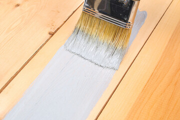 Brush with can paint in hand. A man paints wooden boards in a gray paint brush.