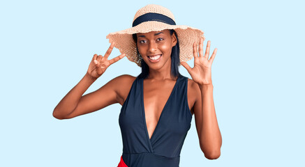 Obraz na płótnie Canvas Young african american woman wearing swimsuit and summer hat showing and pointing up with fingers number seven while smiling confident and happy.