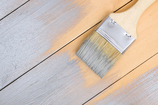 Brush with can paint in hand. A man paints wooden boards in a gray paint brush.