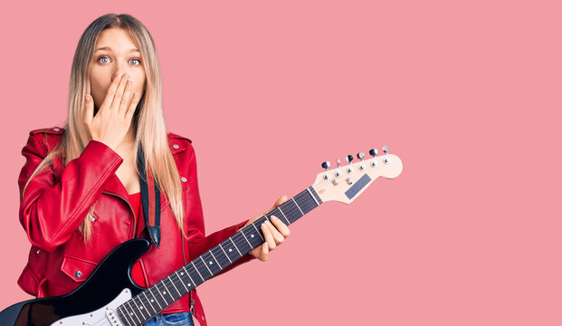 Young beautiful blonde woman playing electric guitar covering mouth with hand, shocked and afraid for mistake. surprised expression