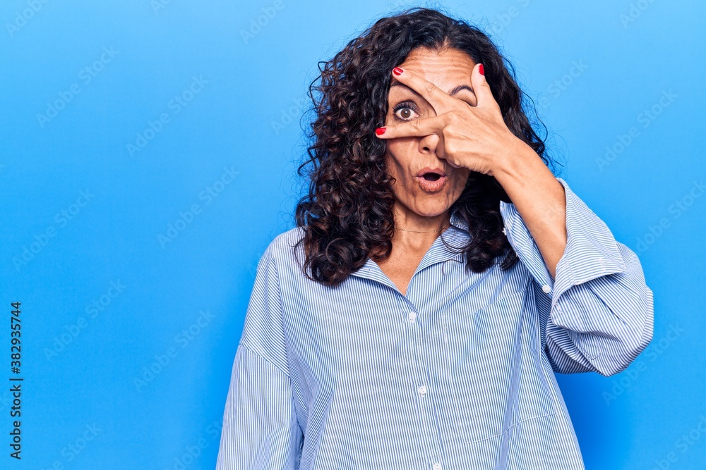 Wall mural middle age beautiful woman wearing casual shirt peeking in shock covering face and eyes with hand, l