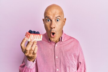 Middle age bald man holding cheesecake scared and amazed with open mouth for surprise, disbelief...