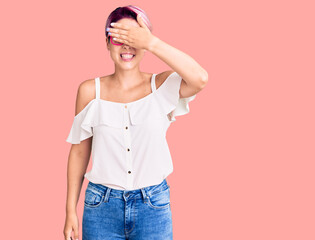 Young beautiful woman with pink hair wearing casual clothes and glasses smiling and laughing with hand on face covering eyes for surprise. blind concept.