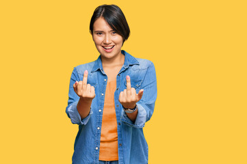 Young beautiful hispanic woman with short hair wearing casual denim jacket showing middle finger...