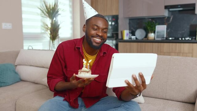 Happy birthday African man celebrating holiday for one at home communicating via tablet videochat conference webcam call connecting with family. Birthday alone. Social distance. Quarantine concept.