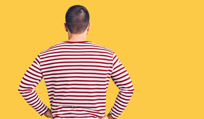 Young handsome man wearing striped sweater standing backwards looking away with arms on body