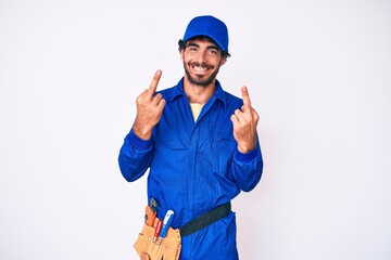 Handsome young man with curly hair and bear weaing handyman uniform showing middle finger doing fuck you bad expression, provocation and rude attitude. screaming excited