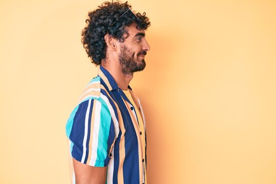 Handsome young man with curly hair and bear wearing summer shirt and sunglasses looking to side, relax profile pose with natural face with confident smile.