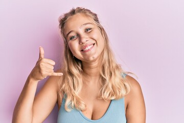 Young blonde girl wearing casual clothes smiling doing phone gesture with hand and fingers like talking on the telephone. communicating concepts.