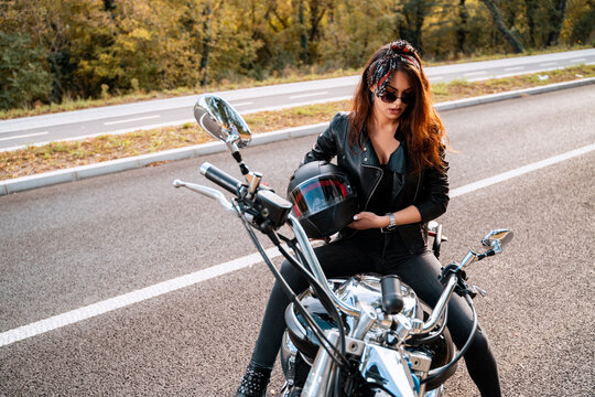 Attractive girl holding bike helmet in her hands while sitting on bike on the road, unposed