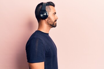 Young hispanic man listening to music using headphones looking to side, relax profile pose with...