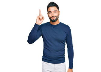 Fototapeta premium Young man with beard wearing casual blue winter sweater pointing finger up with successful idea. exited and happy. number one.