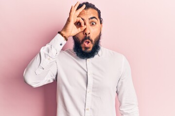 Young arab man wearing casual clothes doing ok gesture shocked with surprised face, eye looking through fingers. unbelieving expression.