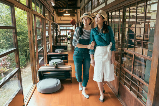 Travel Lifestyle Moments In Traditional Japanese House. Full Length Group Young Female Tourists Wearing Socks Walking On Wooden Floor Inside Ancient Wood Building. Women Together Looking Outdoors