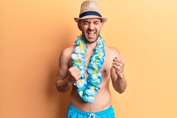 Young handsome bald man shirtless wearing swimwear and hawaiian lei celebrating surprised and...