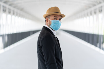 Young asian casual businessman wearing hat and protection mask standing on walkway airport terminal. Safety travel concept..