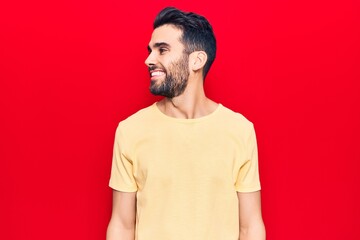 Young handsome man with beard wearing casual t-shirt looking away to side with smile on face, natural expression. laughing confident.