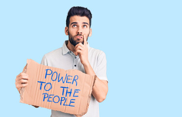 Young handsome man with beard holding power to the people cardboard banner serious face thinking...