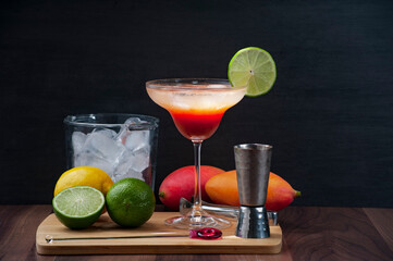 Cocktail of mango, vodka, lemon and ice. On a wooden board accompanied by an ice bucket. Copy space