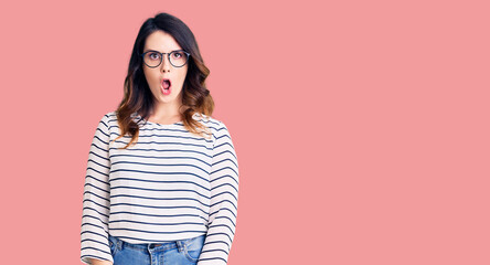 Obraz premium Beautiful young brunette woman wearing casual clothes and glasses afraid and shocked with surprise expression, fear and excited face.