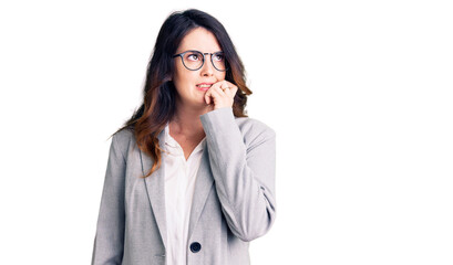 Beautiful young brunette woman wearing business clothes and glasses looking stressed and nervous with hands on mouth biting nails. anxiety problem.