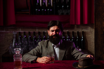 Man with beard holds glass brandy, drink cognac in pub. Guy hipster tastes drink. Sipping whiskey. Luxury nightlife, rich bearded man drink expensive beverage.