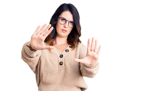 Beautiful young brunette woman wearing casual clothes and glasses doing stop gesture with hands palms, angry and frustration expression