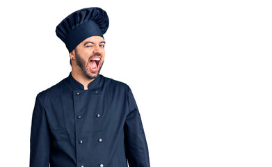 Young hispanic man wearing cooker uniform winking looking at the camera with sexy expression,...