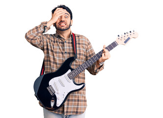 Young hispanic man playing electric guitar stressed and frustrated with hand on head, surprised and angry face